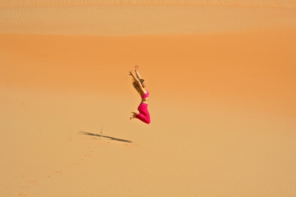 Kara dressed in hot pink jumping in the sand.
